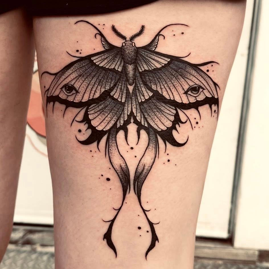 Black butterfly tattoo on a person's leg with a blurred background