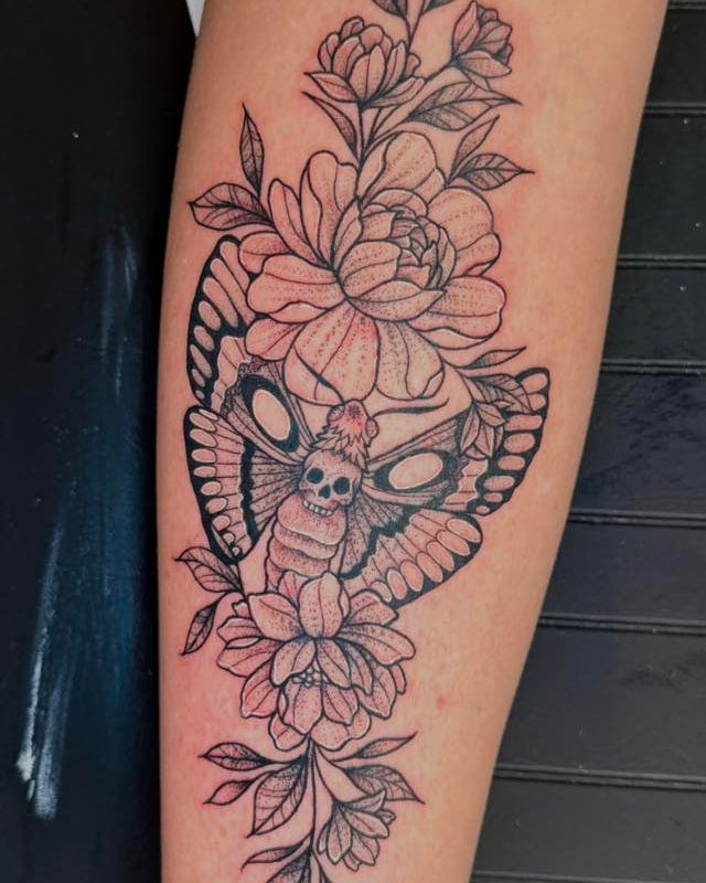 Tattoo of a owl and floral design on a person's arm against a dark background