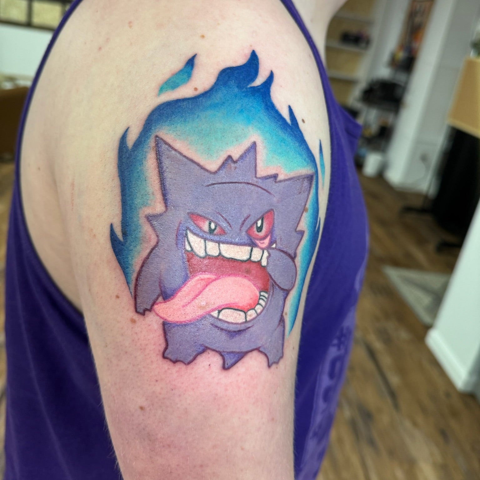 Tattoo of a cartoon character on a person's arm, with a blurred indoor background.